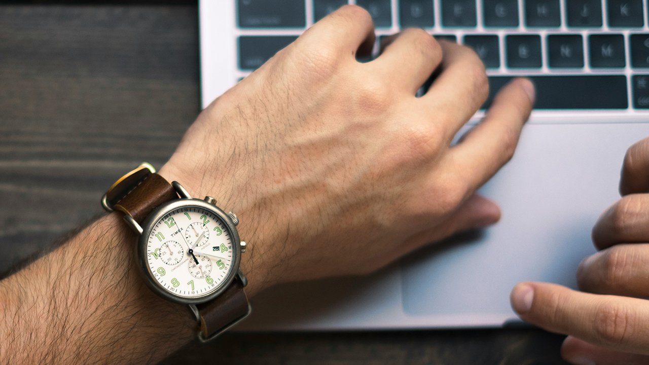 man looking at his watch as he uses a laptop